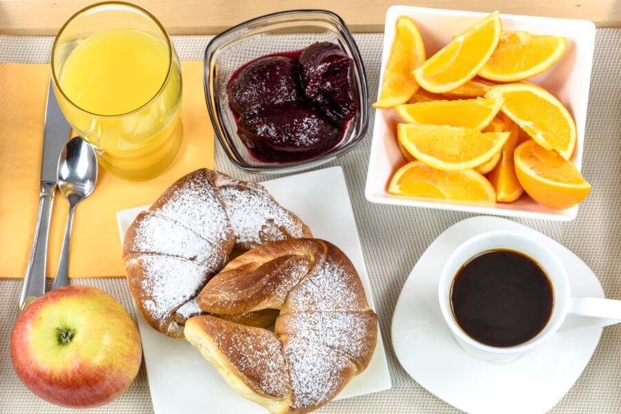 Overhead shot on hotel's breakfast tray with croissants, coffee, oranges, juice, jam, apple and cutlery